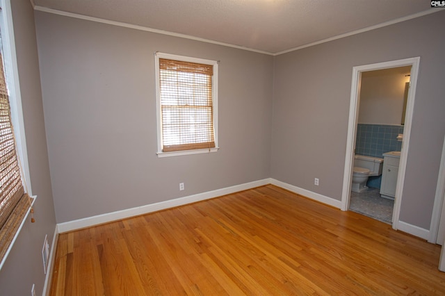 unfurnished bedroom featuring ornamental molding, connected bathroom, and light hardwood / wood-style flooring