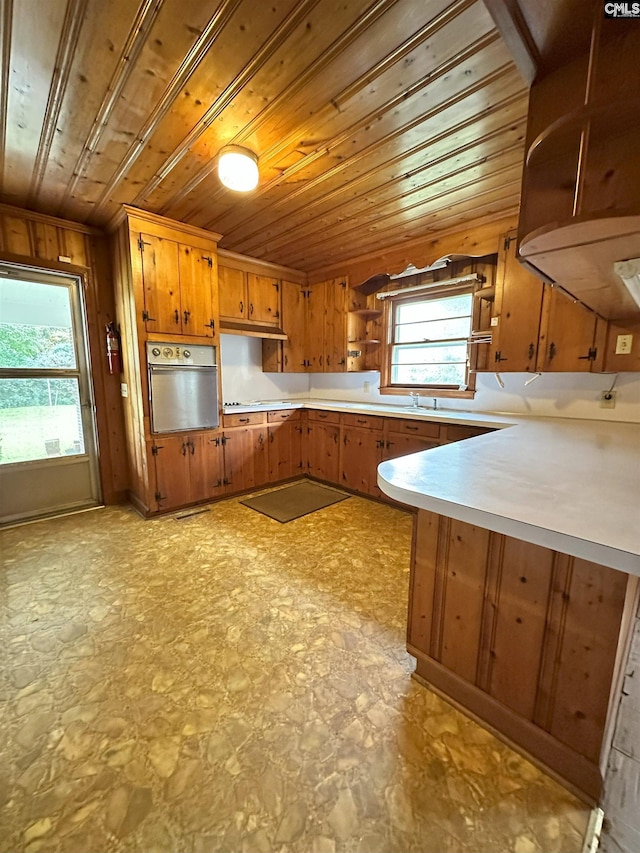 kitchen featuring sink, kitchen peninsula, wood walls, oven, and wood ceiling