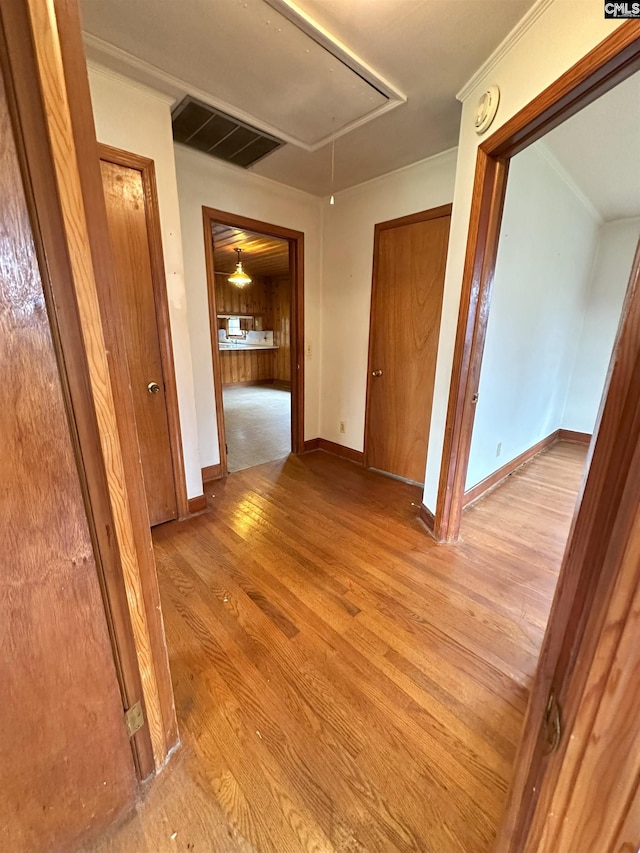 hallway featuring wood walls, ornamental molding, and light wood-type flooring