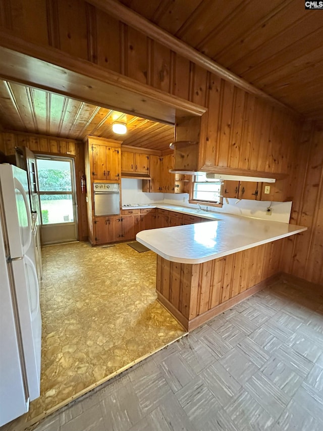 kitchen with wood walls, white appliances, kitchen peninsula, and wooden ceiling