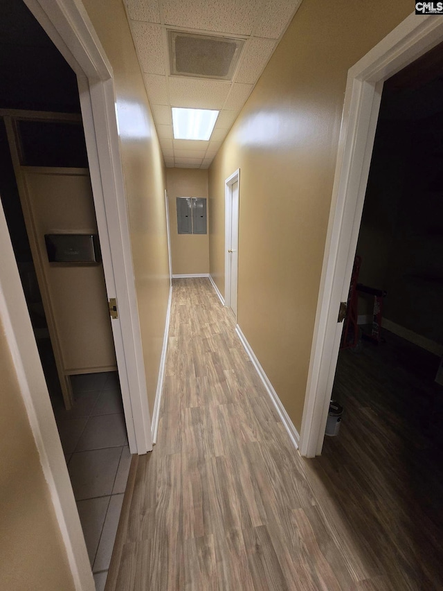 hall with wood-type flooring, a paneled ceiling, and electric panel