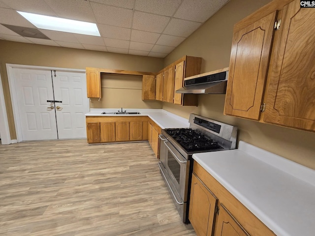 kitchen with a paneled ceiling, stainless steel gas range oven, sink, light wood-type flooring, and extractor fan