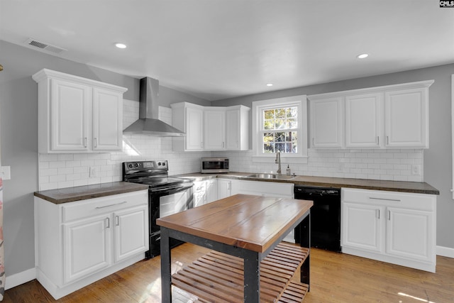 kitchen with black appliances, white cabinets, wall chimney range hood, sink, and light hardwood / wood-style floors