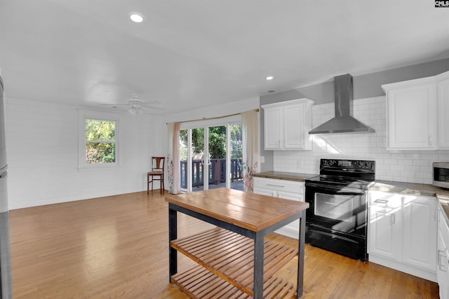 kitchen featuring decorative backsplash, black electric range oven, wall chimney range hood, light hardwood / wood-style floors, and white cabinetry