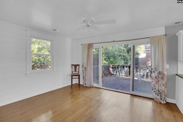 unfurnished room featuring hardwood / wood-style flooring, plenty of natural light, ceiling fan, and wood walls