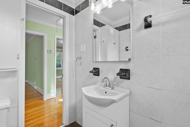 bathroom with wood-type flooring, toilet, vanity, tile walls, and ornamental molding