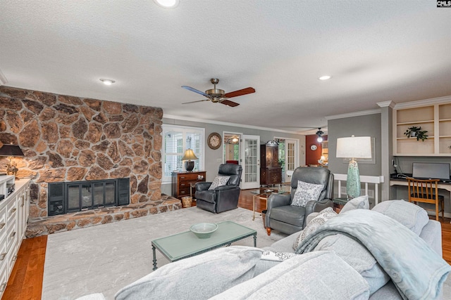 living room featuring ceiling fan, wood-type flooring, a textured ceiling, a fireplace, and ornamental molding