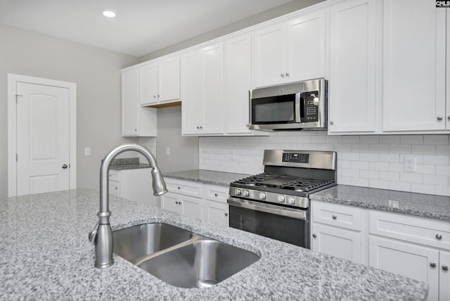 kitchen with white cabinets, sink, tasteful backsplash, light stone counters, and stainless steel appliances