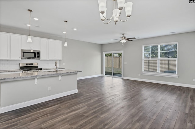 kitchen with dark wood-type flooring, appliances with stainless steel finishes, decorative light fixtures, light stone counters, and white cabinetry