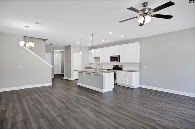 kitchen with dark hardwood / wood-style floors, pendant lighting, a kitchen island with sink, white cabinets, and appliances with stainless steel finishes