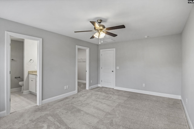 unfurnished bedroom with connected bathroom, ceiling fan, a walk in closet, light carpet, and a closet