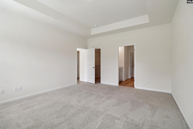 unfurnished bedroom featuring connected bathroom, light colored carpet, and a raised ceiling
