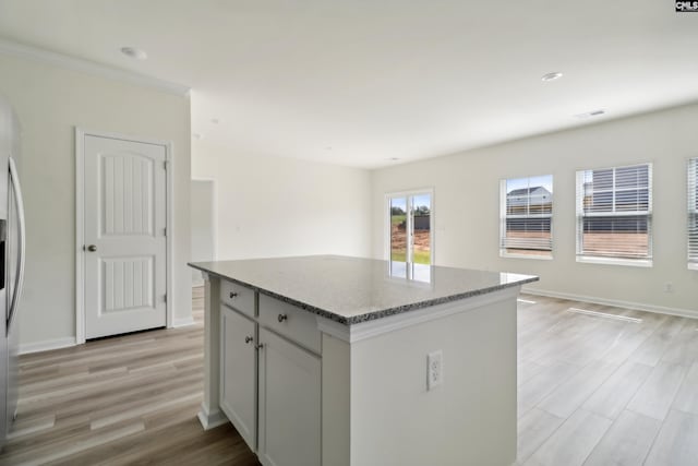 kitchen with stainless steel fridge, a kitchen island, light stone counters, and light wood-type flooring