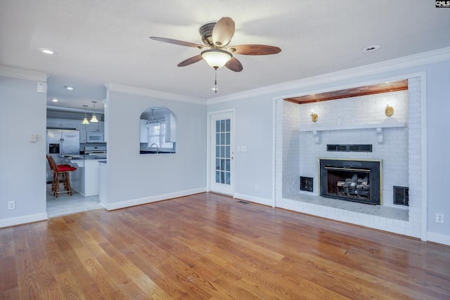 unfurnished living room featuring ceiling fan, light hardwood / wood-style floors, crown molding, and a fireplace