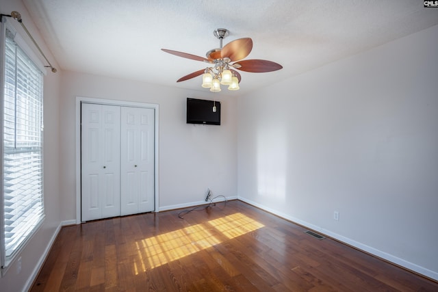 unfurnished bedroom featuring multiple windows, dark wood-type flooring, and ceiling fan