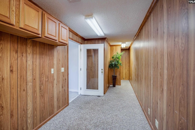 corridor featuring light colored carpet, ornamental molding, a textured ceiling, and wooden walls