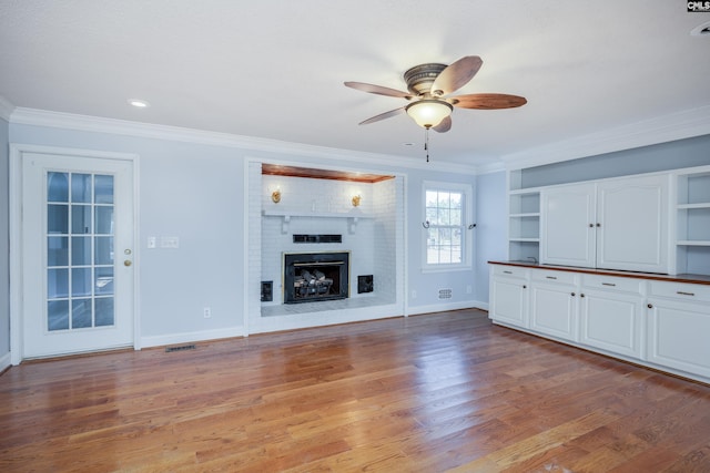 unfurnished living room with crown molding, a brick fireplace, ceiling fan, built in features, and light hardwood / wood-style floors