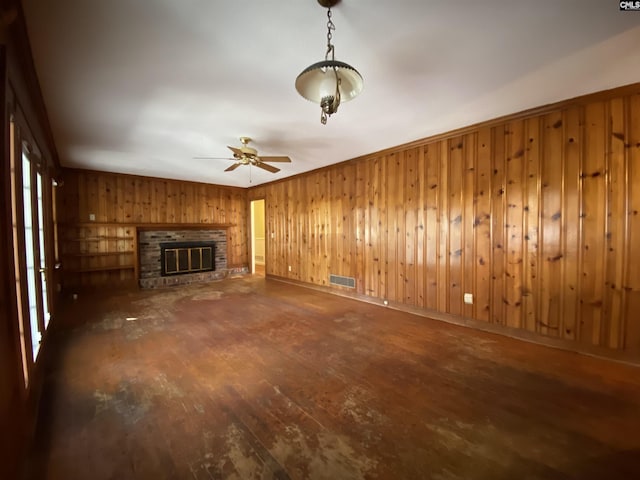 unfurnished living room featuring dark hardwood / wood-style flooring, a brick fireplace, ceiling fan, and wooden walls