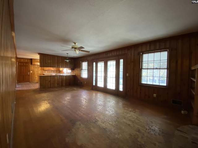 unfurnished living room featuring wood-type flooring, french doors, ceiling fan, and wooden walls