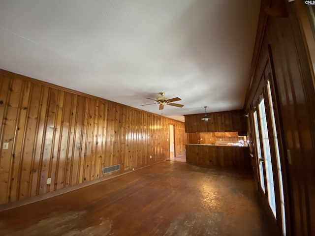 unfurnished living room featuring ceiling fan, wood walls, and dark wood-type flooring