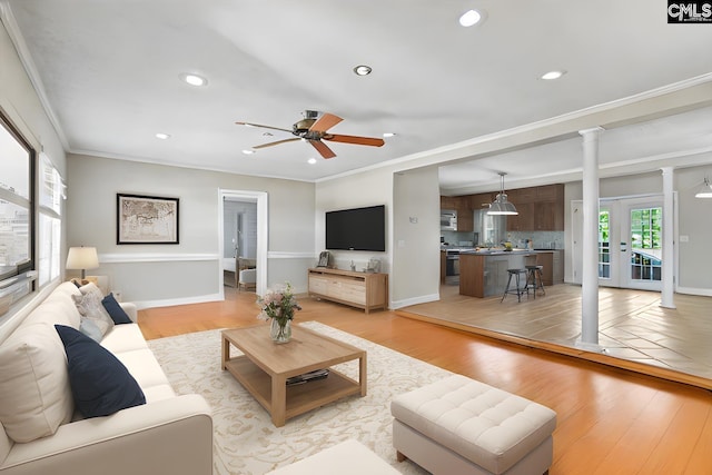 living room with decorative columns, ceiling fan, light hardwood / wood-style floors, and ornamental molding