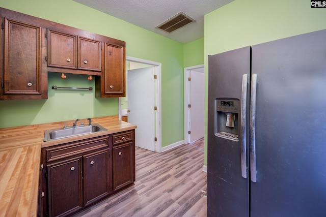 kitchen featuring sink, black fridge, light hardwood / wood-style flooring, butcher block countertops, and a textured ceiling