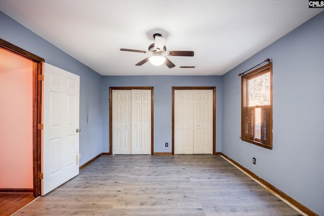 unfurnished bedroom with multiple closets, ceiling fan, light hardwood / wood-style flooring, and a textured ceiling