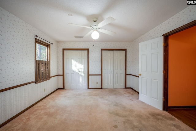 unfurnished bedroom featuring two closets, ceiling fan, carpet floors, and a textured ceiling