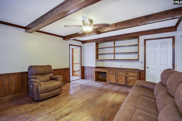 living room featuring ceiling fan, wooden walls, wood-type flooring, built in desk, and beamed ceiling