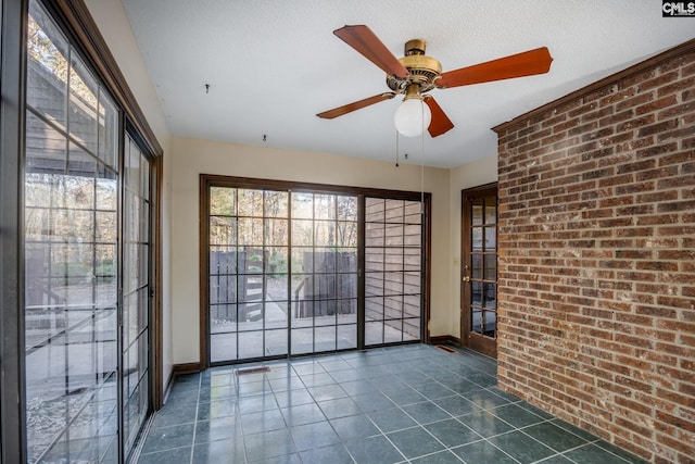 tiled empty room featuring a textured ceiling, ceiling fan, and brick wall