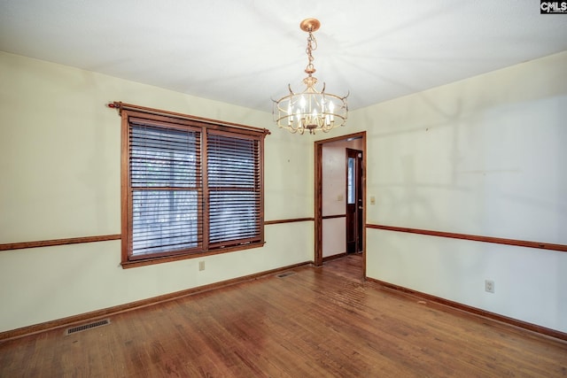 spare room with a notable chandelier and wood-type flooring