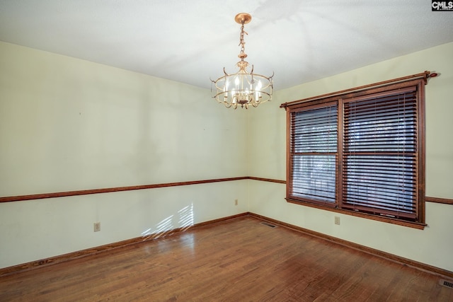 empty room with hardwood / wood-style floors and a notable chandelier