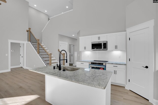 kitchen with white cabinetry, a towering ceiling, stainless steel appliances, and a kitchen island with sink