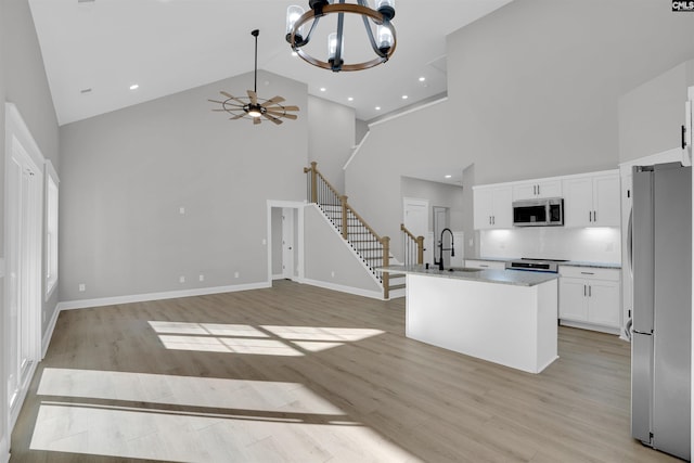 kitchen featuring sink, high vaulted ceiling, an island with sink, appliances with stainless steel finishes, and light wood-type flooring