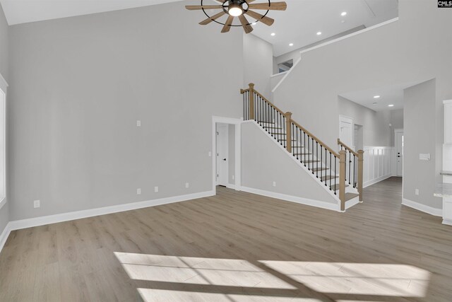 unfurnished living room with ceiling fan, light hardwood / wood-style flooring, and a high ceiling