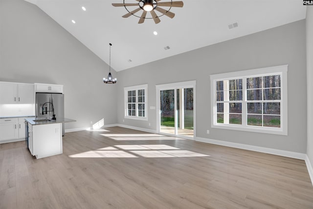 unfurnished living room with ceiling fan with notable chandelier, light hardwood / wood-style floors, high vaulted ceiling, and sink