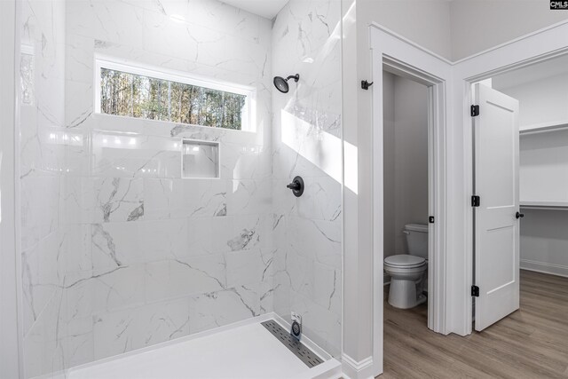 bathroom featuring toilet, a tile shower, and wood-type flooring