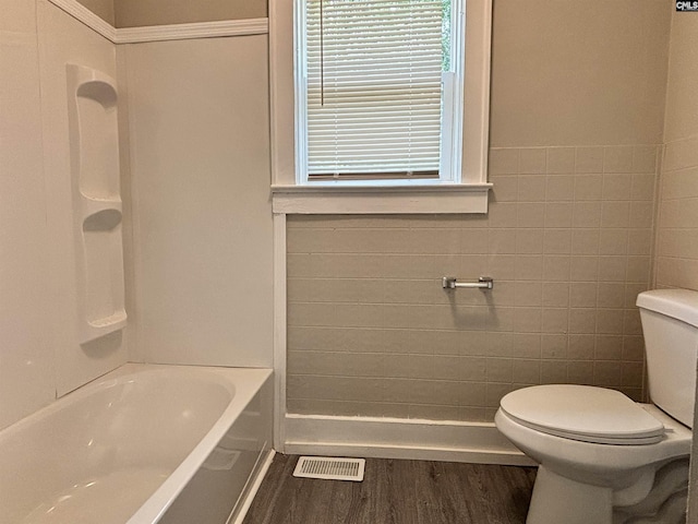 bathroom featuring hardwood / wood-style floors, shower / bathing tub combination, toilet, and tile walls