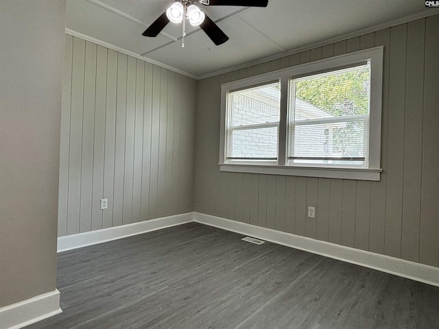 spare room featuring crown molding, wooden walls, ceiling fan, and dark hardwood / wood-style floors