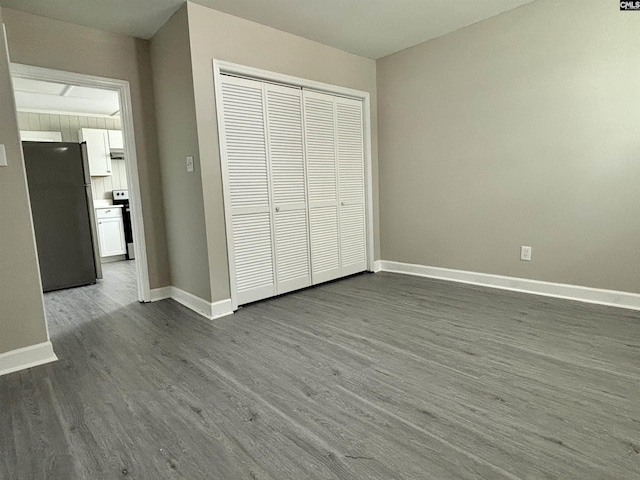 unfurnished bedroom with stainless steel refrigerator, a closet, and hardwood / wood-style flooring