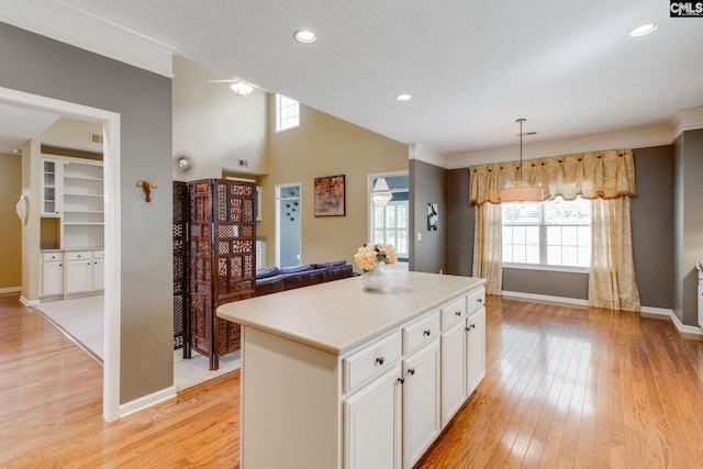 kitchen featuring white cabinets, open floor plan, a center island, decorative light fixtures, and light countertops