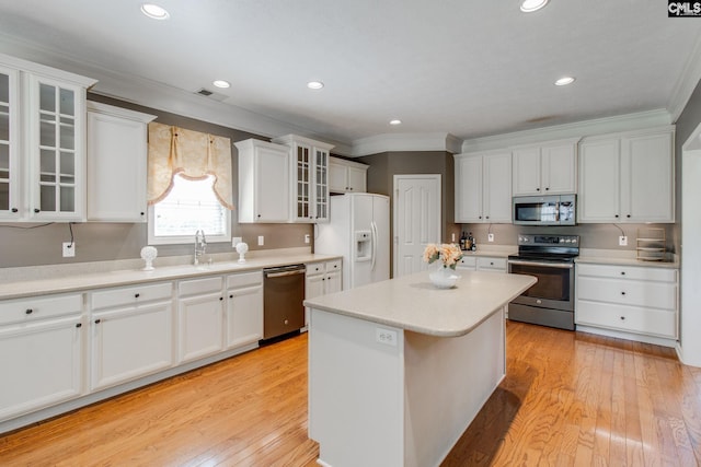 kitchen with a kitchen island, glass insert cabinets, appliances with stainless steel finishes, light countertops, and white cabinetry