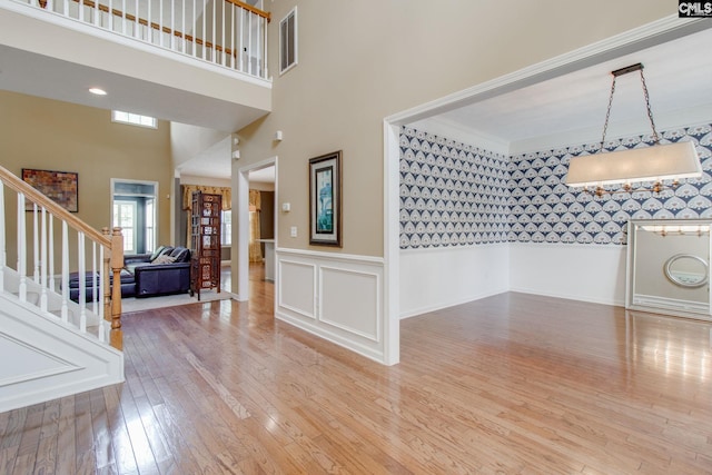 foyer featuring visible vents, stairway, light wood-style flooring, a towering ceiling, and wainscoting