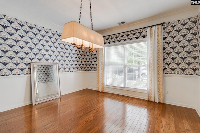 unfurnished dining area with ornamental molding, wood finished floors, visible vents, and wallpapered walls