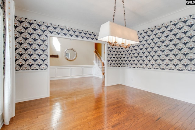 spare room featuring a wainscoted wall, crown molding, wallpapered walls, wood finished floors, and stairs