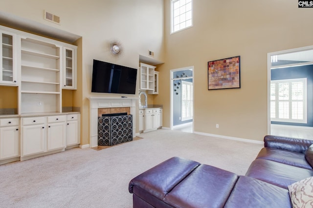 living area featuring a tile fireplace, light colored carpet, a towering ceiling, baseboards, and visible vents