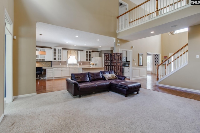 living area with baseboards, a towering ceiling, a wealth of natural light, and light colored carpet