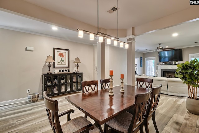 dining space with decorative columns, ceiling fan, crown molding, and light wood-type flooring