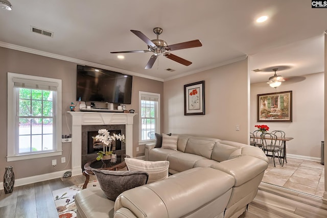 living room with plenty of natural light, light wood-type flooring, crown molding, and a high end fireplace