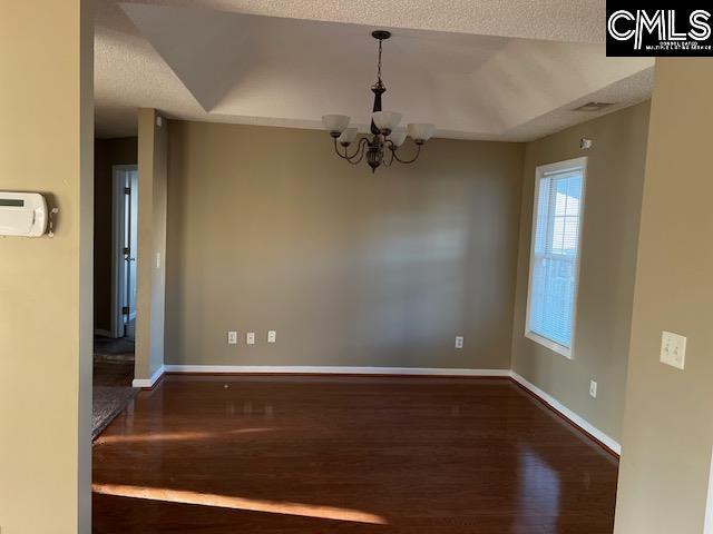 empty room with dark hardwood / wood-style flooring, a textured ceiling, and a notable chandelier